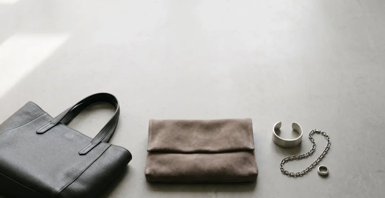 Minimalist composition of structured neutral accessories including leather bag and metallic details against clean background