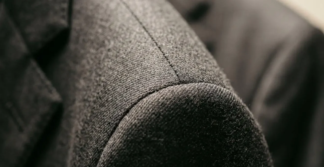 Extreme close-up macro detail of blazer shoulder seam construction showing fabric grain and stitching precision on wool suiting